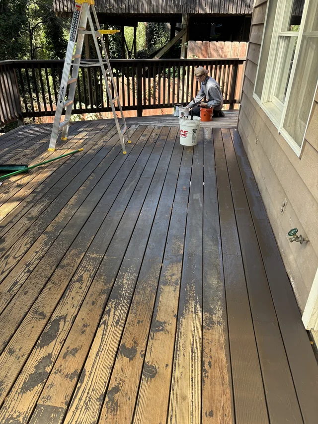 A crew member works beside coating containers on a weathered wood deck during preparation.