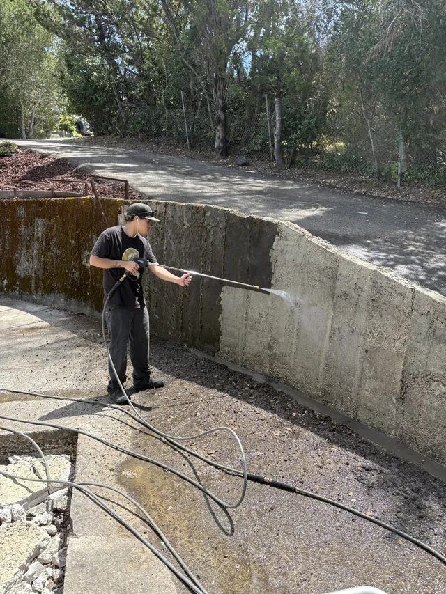 A crew member pressure-washes the surface of a masonry retaining wall.